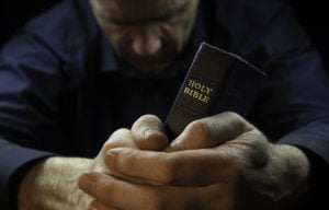 A Man Praying Holding A Holy Bible.