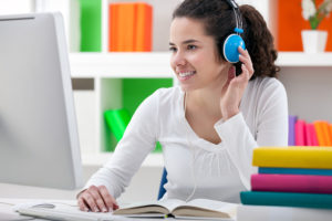teen girl doing her homework online and listening to headphones.
